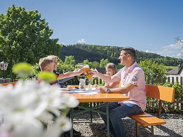 Biergarten, Familie mit zwei jüngeren Kindern prostet sich zu, Blume und Umgebung mit Aussicht